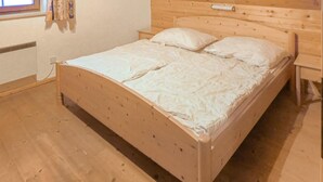 A wooden bed with a headboard, white bedding, and a window with curtains. - Ferienhaus mit Bergpanorama (Ebensee)