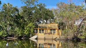 Una cabaña de madera con cerramiento de vidrio, rodeada de vegetación densa y reflejada en el agua.