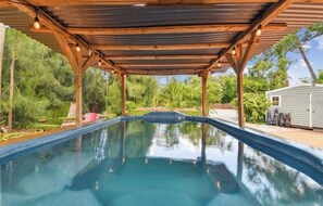 Une piscine surmontée d’une pergola en bois, entourée de verdure.