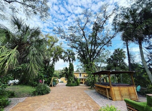 A garden area with a brick pathway leading to a wooden structure, surrounded by various trees and plants.
