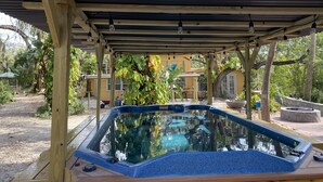 Un jacuzzi bajo una pérgola de madera con una piscina al fondo.