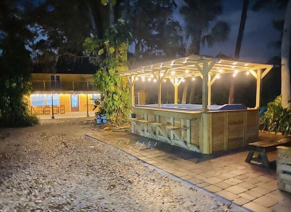A wooden gazebo with string lights, a wooden bench, and a paved area with potted plants. - Sleeps 20+, 2 houses, Swim-Spa, hot tub, bachelor and party place (Tampa)