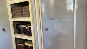 Una habitación con un armario blanco, un estante con toallas dobladas y una cesta en el suelo.