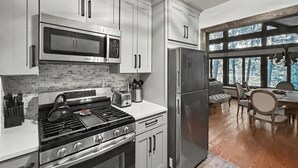 A modern kitchen with stainless steel appliances, a brick backsplash, and a dining area with a view. - Private Lake Front Adirondack Retreat on Loon Lake-20 Min from Lake George, Gore (Chestertown)