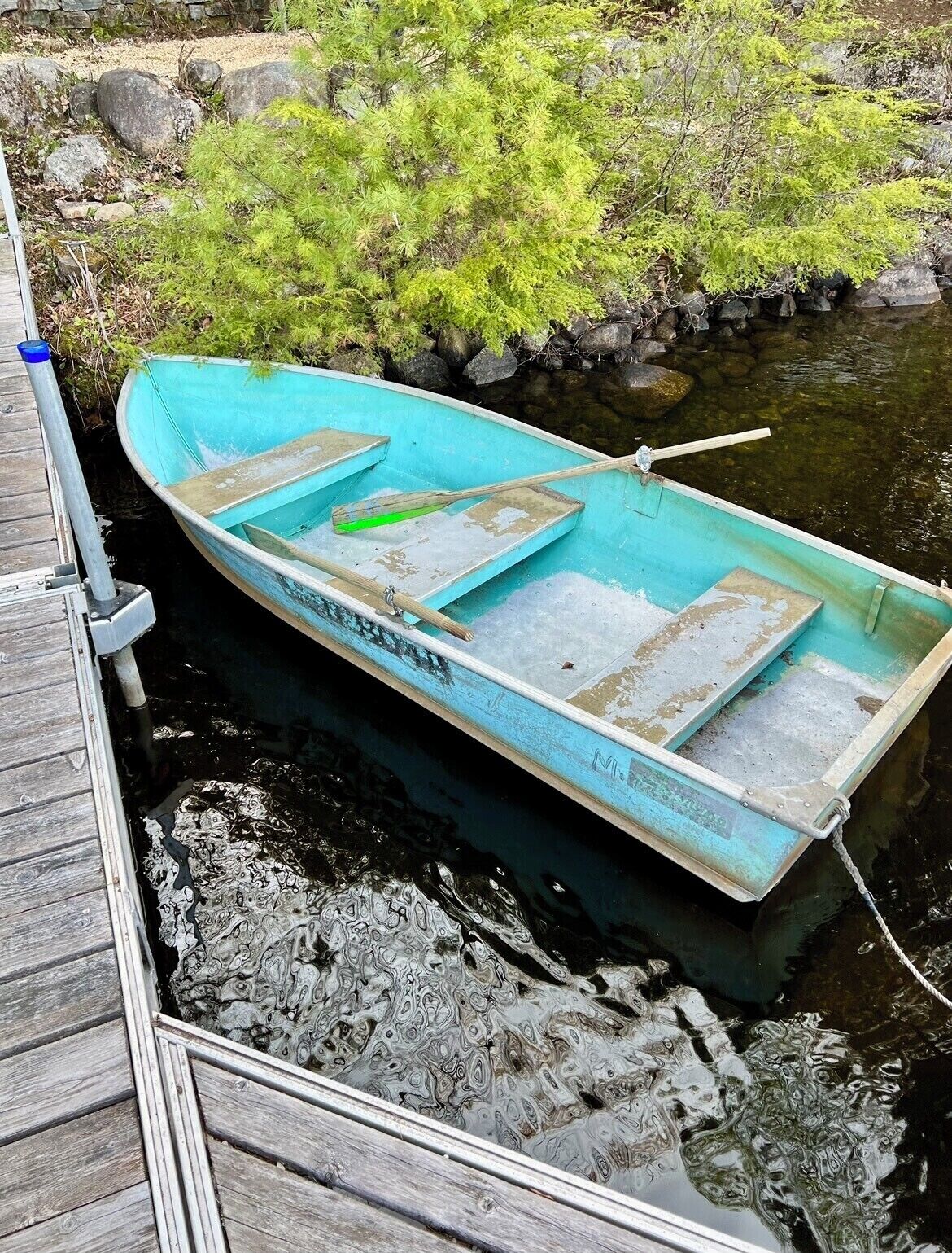 Um pequeno barco azul-turquesa atracado num cais de madeira.