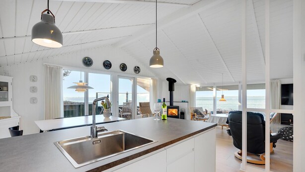 Een moderne keuken met een groot eiland, een RVS-gootsteen en hangende lampen.