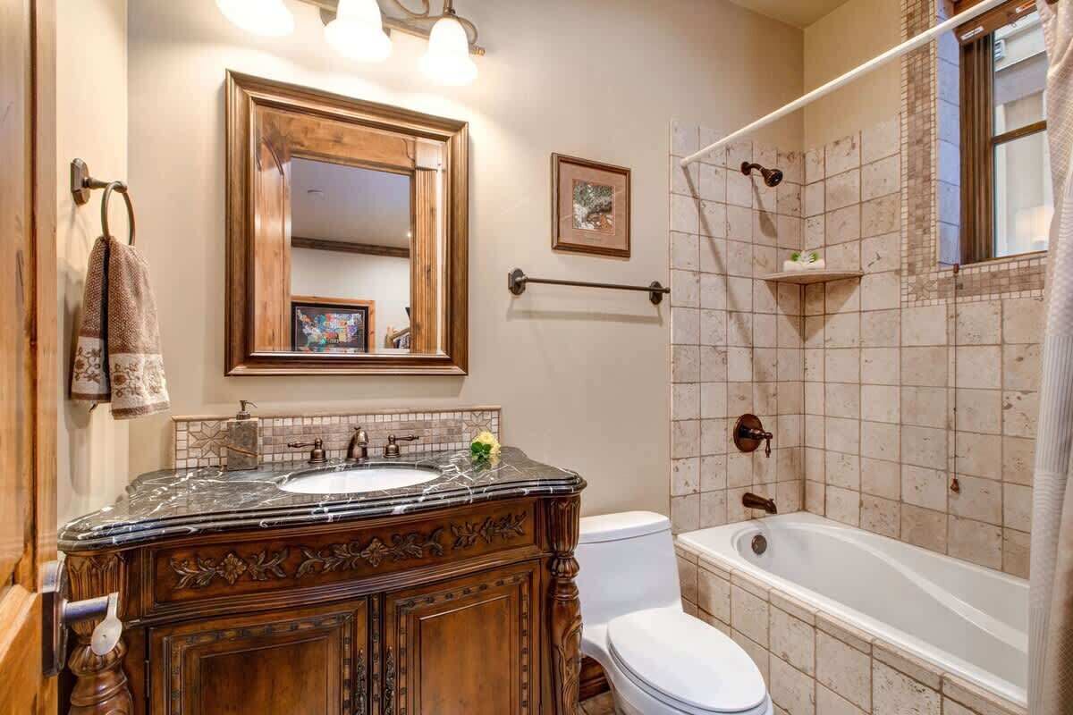 Een badkamer met een houten wastafelmeubel, een grote spiegel, een bad en een toilet.
