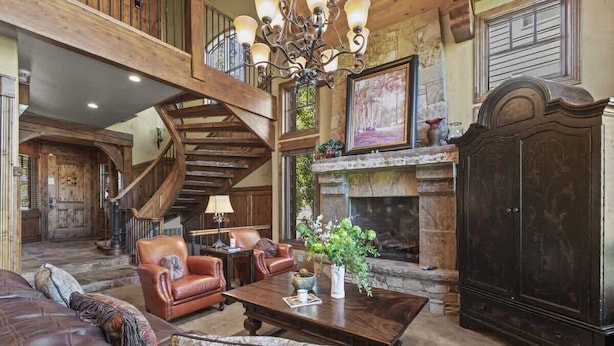 Un salon spacieux doté d’une cheminée, de meubles en cuir, d’un escalier en bois et d’une grande armoire.