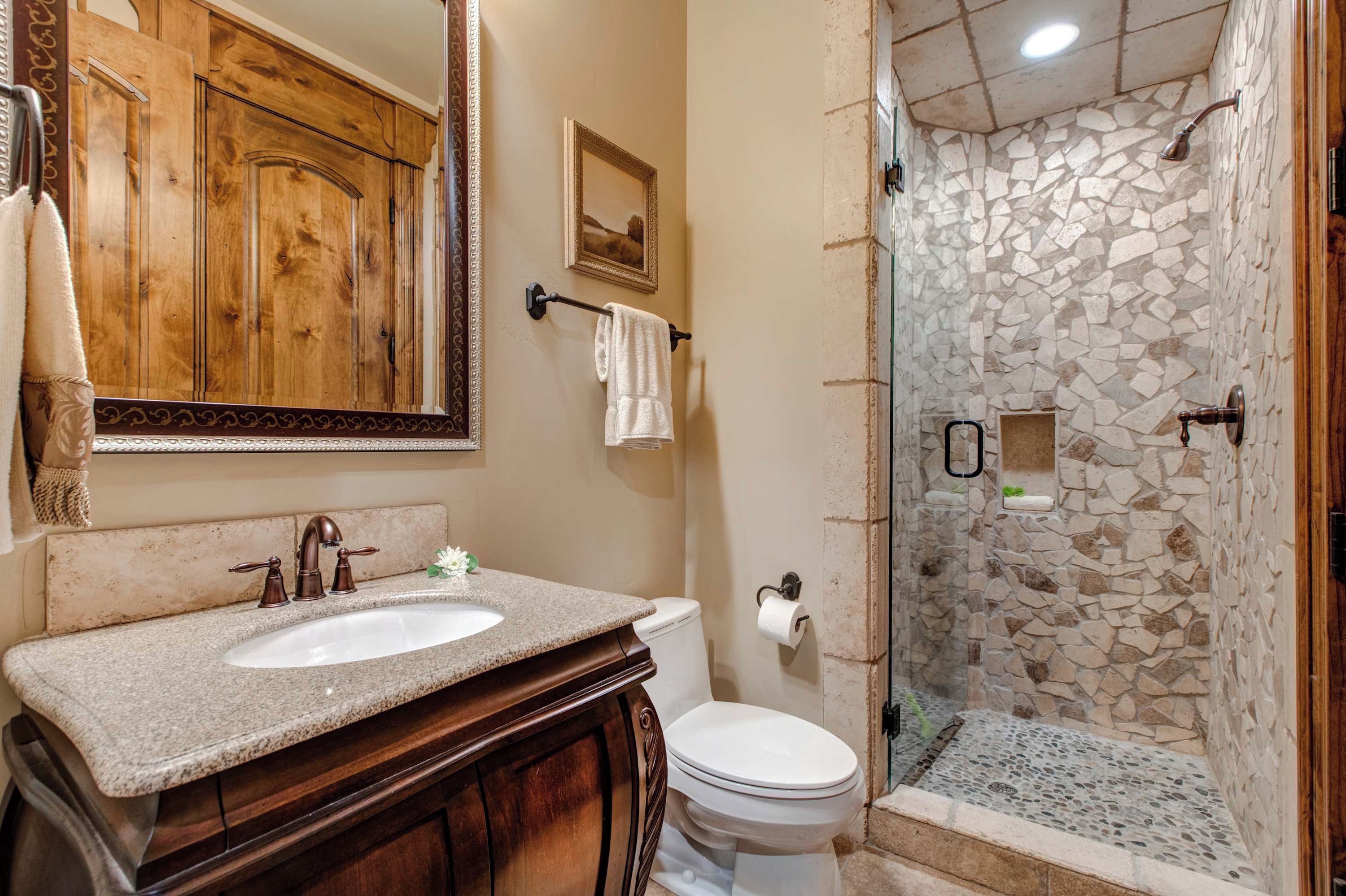 Un baño con tocador de madera, lavamanos, inodoro y ducha con pared de piedra.