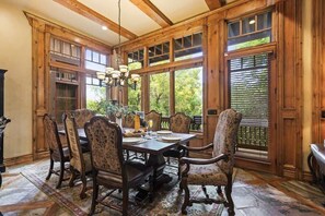 A dining area with a wooden table, upholstered chairs, and large windows with blinds. - Abode at Angus House, private hot tub, at PCMR base (Park City)