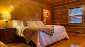 Ein gemütliches Schlafzimmer einer Holzhütte mit Bett, Nachttisch und einem Fenster mit Jalousien.
