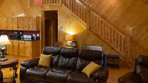 Ein gemütliches Blockhaus-Interieur mit einer Holztreppe, einem Ledersofa und einer Küchenzeile mit Holzausbau.