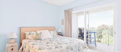 Un dormitorio con cama, mesita de noche, lámpara, ventilador de techo y un balcón con sillas.
