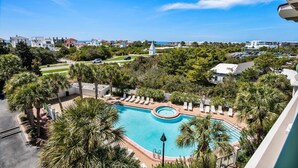 Un resort con una piscina grande rodeada de palmeras y sillas de descanso, con vistas a la costa, edificios y un cielo despejado.