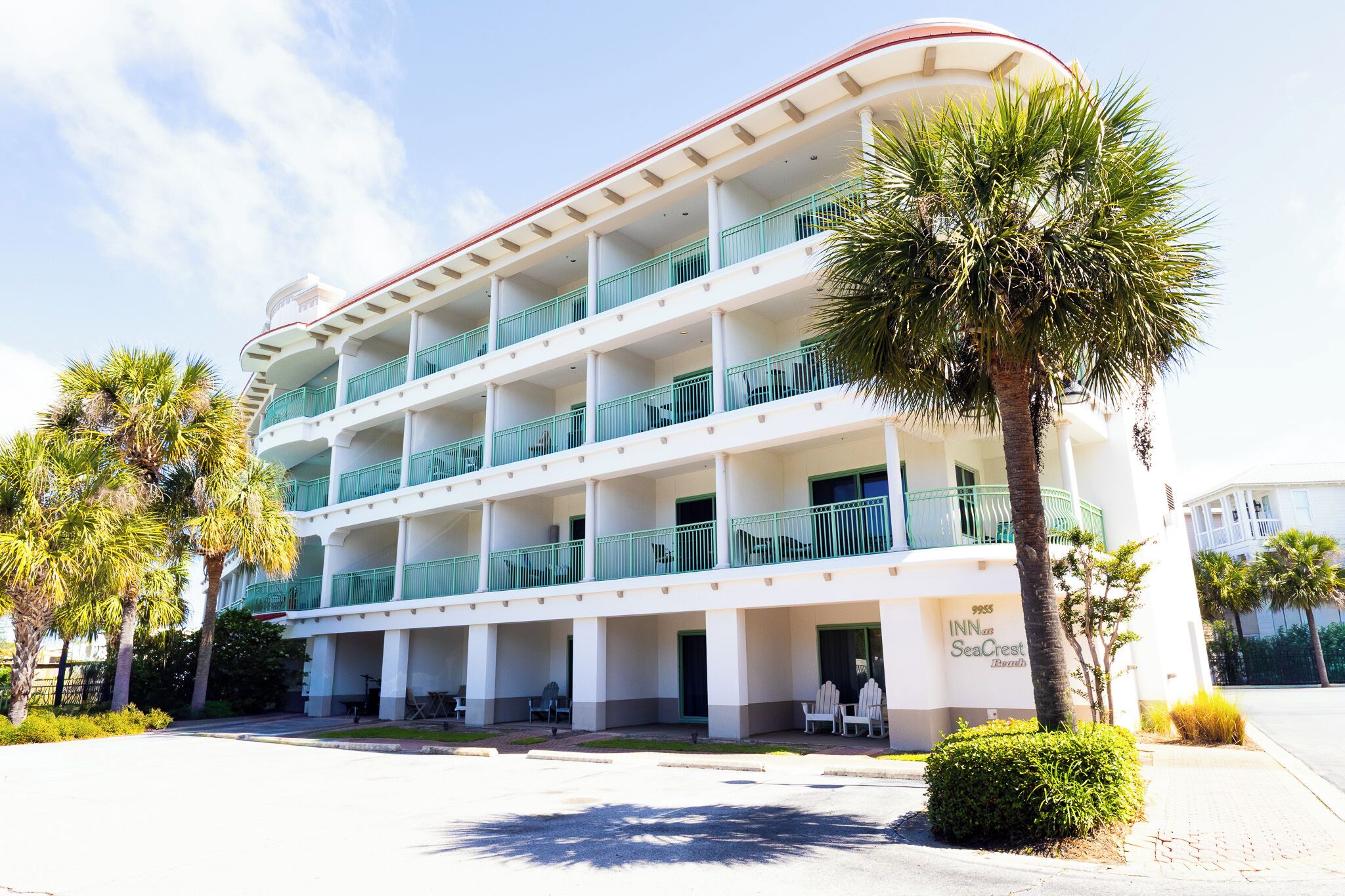 Un hotel de varios pisos con balcones, palmeras y mesas al aire libre.