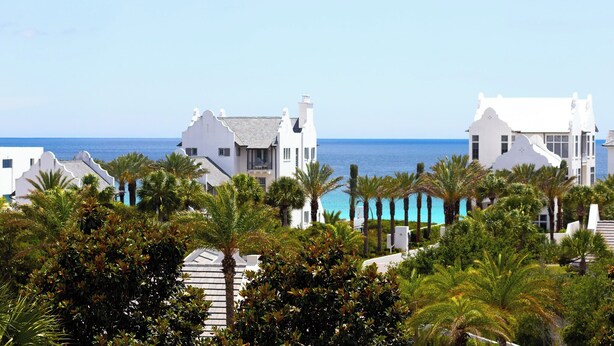 Un resort costero con edificios blancos, palmeras y una vista despejada del océano.