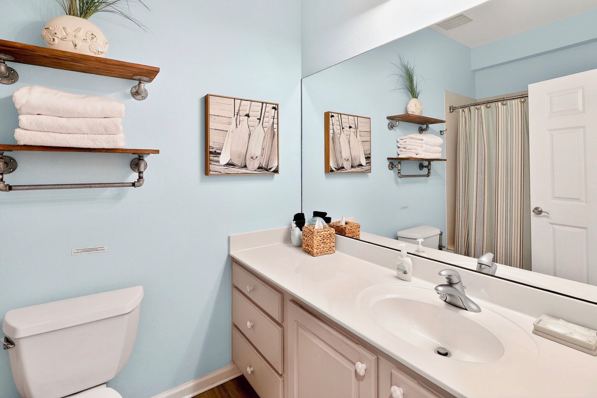 Une salle de bain comprenant des toilettes, un lavabo, un miroir, un porte-serviettes et deux tableaux encadrés accrochés au mur.