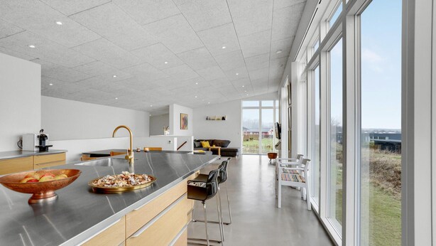 A modern kitchen with a large island, stainless steel countertops, and a view of the outdoors through large windows.