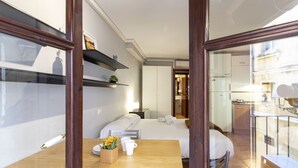 A hotel room with a bed, bedside table, and a view of the kitchen and balcony.