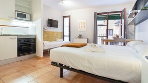 A hotel room with a bed, a desk, a chair, a TV, a microwave, and a kitchen area.