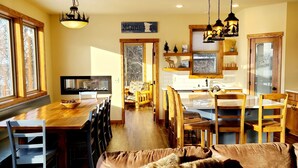 Una sala de estar acogedora con un sofá marrón, una mesa de comedor de madera y una zona de cocina con armarios de madera y un ventanal.