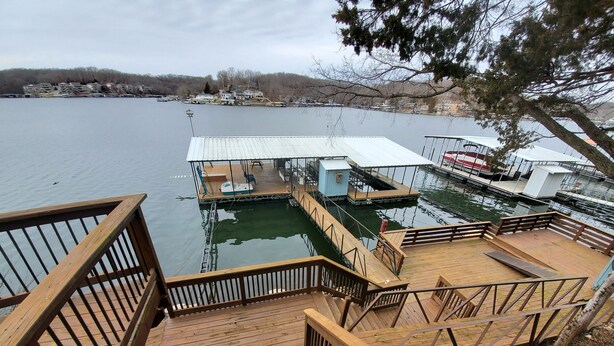 A wooden dock leading to a floating structure with a covered seating area and a small boat. - Lake House with Multiple Decks and Large Swim Platform on Private Dock, (Rocky Mount)