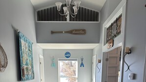 A hallway with a staircase, a decorative wall hanging, and a sign indicating a 'Living on Lake Time' theme. - Lake House with Multiple Decks and Large Swim Platform on Private Dock, (Rocky Mount)