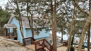 A blue cabin with a wooden staircase leading to a deck, surrounded by trees. - Lake House with Multiple Decks and Large Swim Platform on Private Dock, (Rocky Mount)