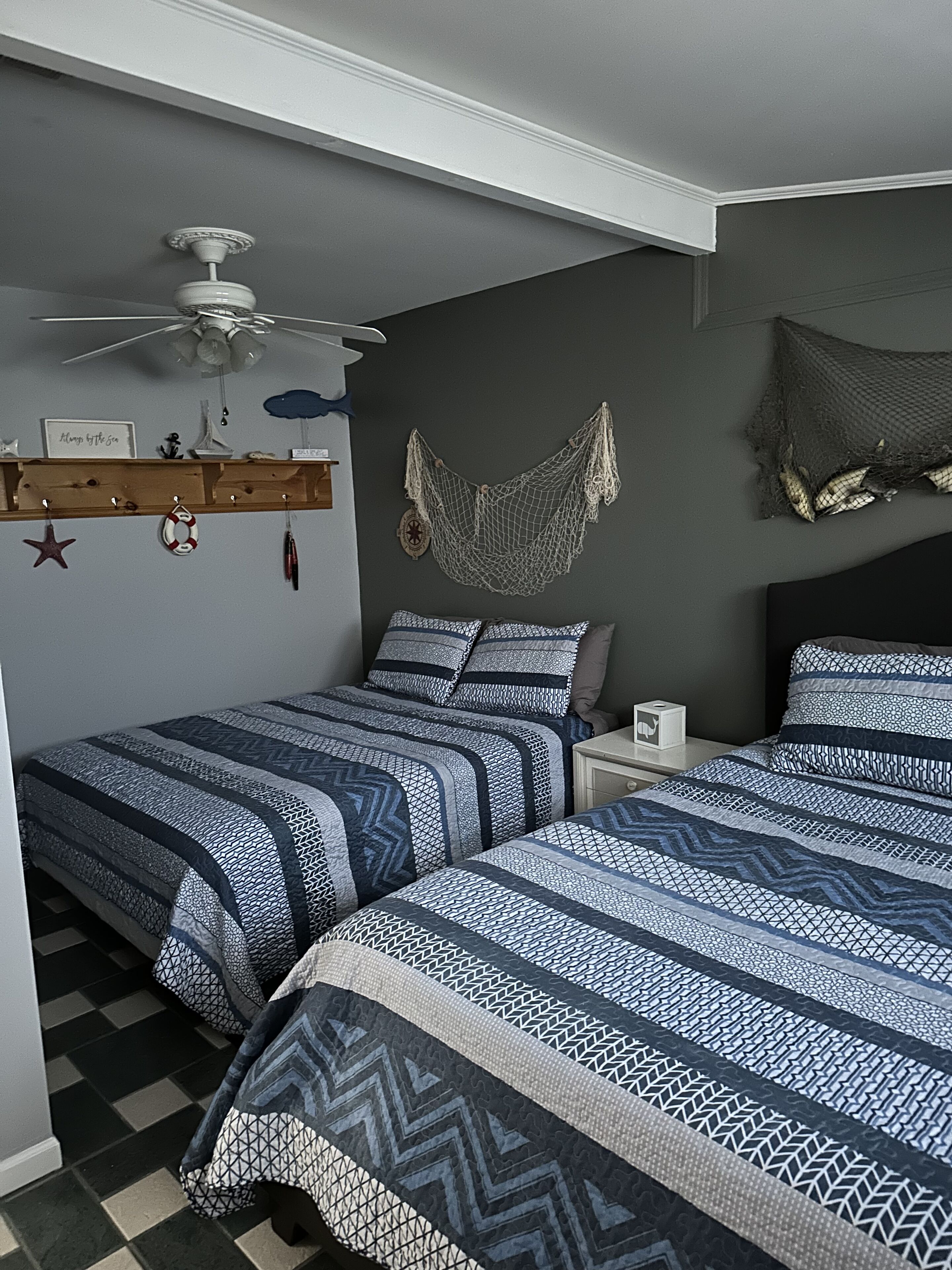 Une chambre avec deux lits, un ventilateur de plafond, un hamac et une étagère ornée d’objets décoratifs.