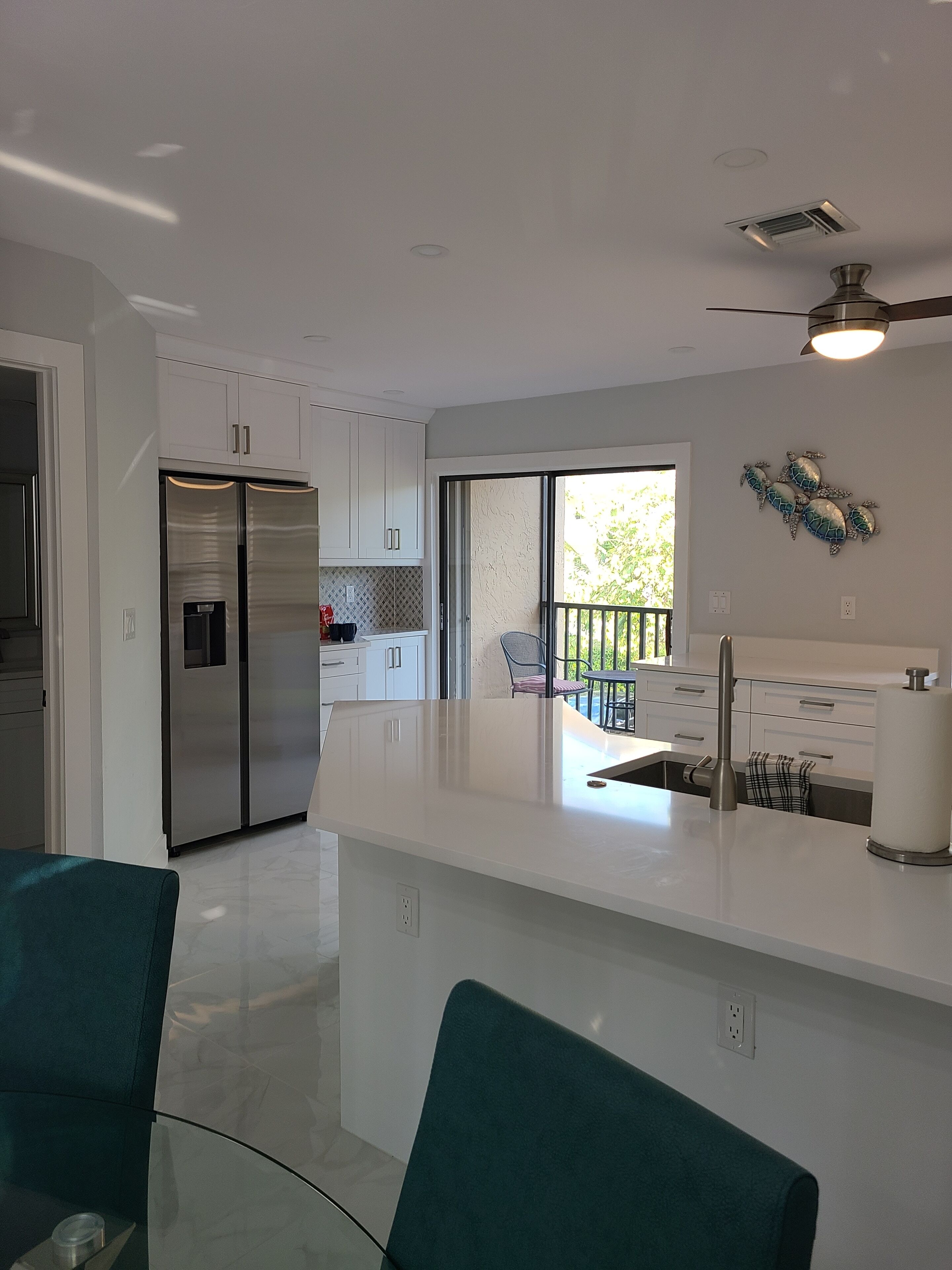 A modern kitchen with white cabinets, a stainless steel refrigerator, and a large island with a sink.