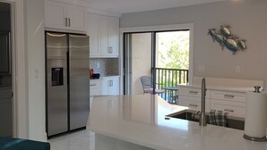 A modern kitchen with white cabinets, a stainless steel refrigerator, and a large island with a sink.