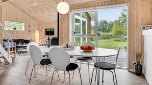 A modern interior with a dining area, wooden walls, and large windows offering a view of the outdoors. - Cozy home in ålbæk with kitchen (Ålbæk)