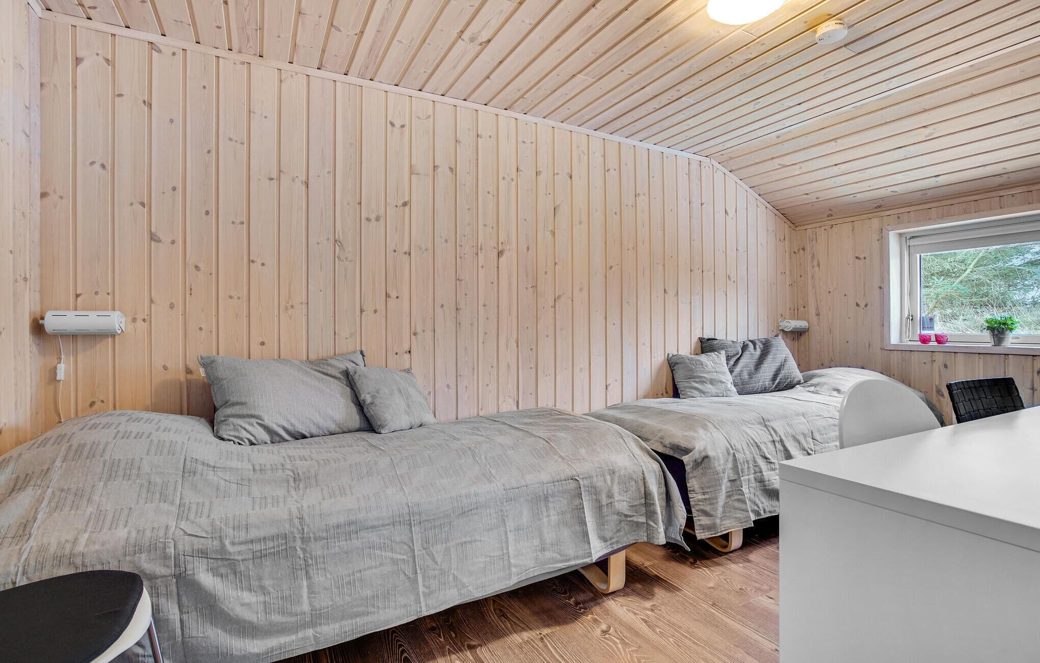 A small, cozy room with two beds, wooden walls, a window with a view, and a small desk.
