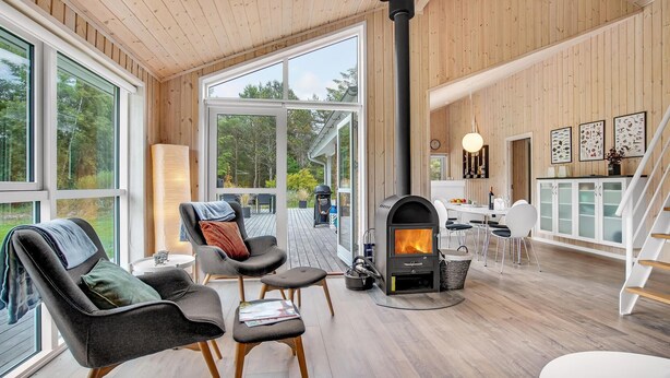 A modern interior with a fireplace, wooden flooring, and large windows offering a view of the outdoors. - Cozy home in ålbæk with kitchen (Ålbæk)