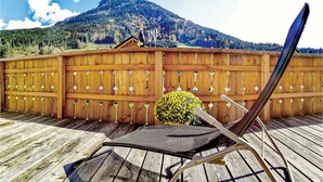 A wooden deck with a chair and a potted plant, overlooking a mountainous landscape.