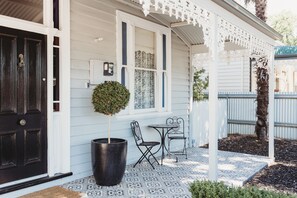 A white house with a black door, a small patio with two metal chairs and a table, and a potted plant. - Hargreaves Cottage - close to CBD (Bendigo)