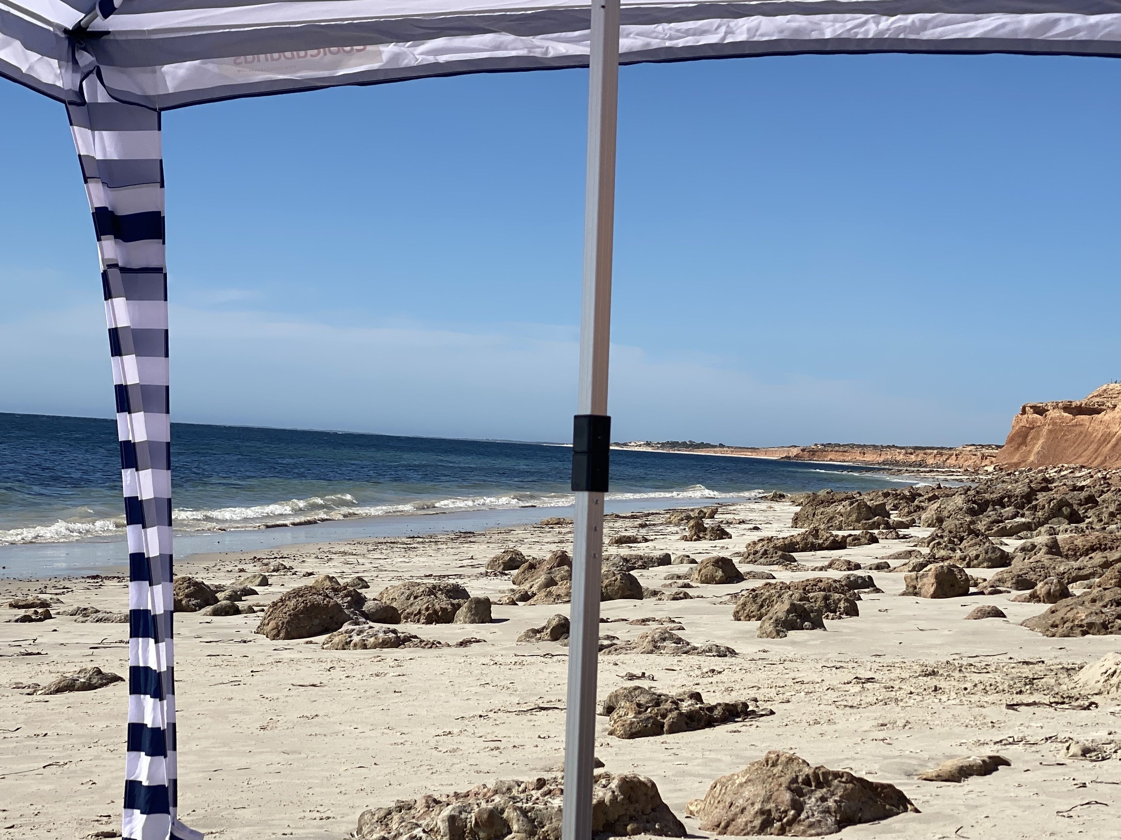 Een strand met een gestreepte luifel en rotsachtig terrein.