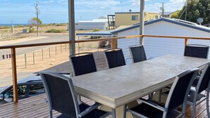 Ett takförsett utomhusområde med bord och stolar, med utsikt över en strand och byggnader.