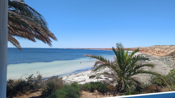En strand med kristallklart blått vatten, en sandstrand och en klippig terräng.
