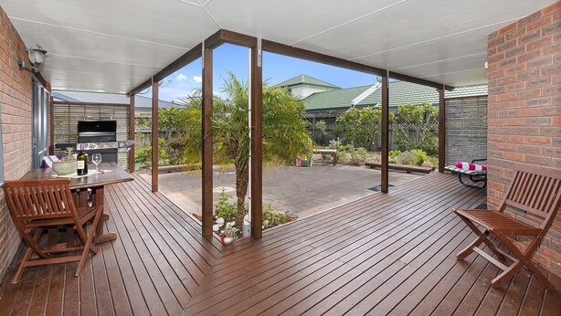 Un patio techado al aire libre con piso de madera, una parrilla y asientos.