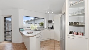 Una cocina moderna con gabinetes blancos, microondas empotrado y refrigerador de acero inoxidable.