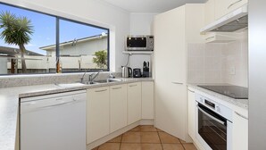 Una cocina moderna con armarios blancos, lavavajillas, microondas, cafetera y estufa.