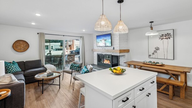 A modern living room with a fireplace, a dining area, and a kitchen island with fruit. - 28th Street Beach House steps to sand, Air Conditioning, beach gear provided!   (Newport Beach)