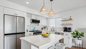 A modern kitchen with white cabinetry, stainless steel appliances, a central island with stools, and pendant lighting. - 28th Street Beach House steps to sand, Air Conditioning, beach gear provided!   (Newport Beach)