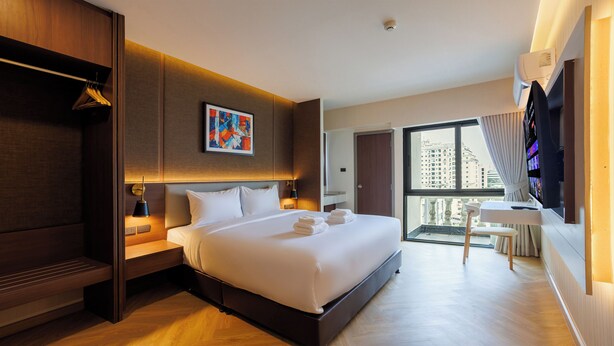 A modern hotel room with a large bed, a desk, a chair, a TV, and a balcony with a city view. - B2 Huai Khwang Boutique & Budget Hotel (Bangkok)