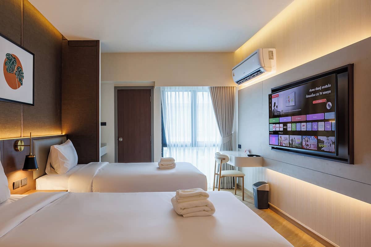 Habitación de hotel con dos camas, un televisor montado en la pared y un cuadro enmarcado.