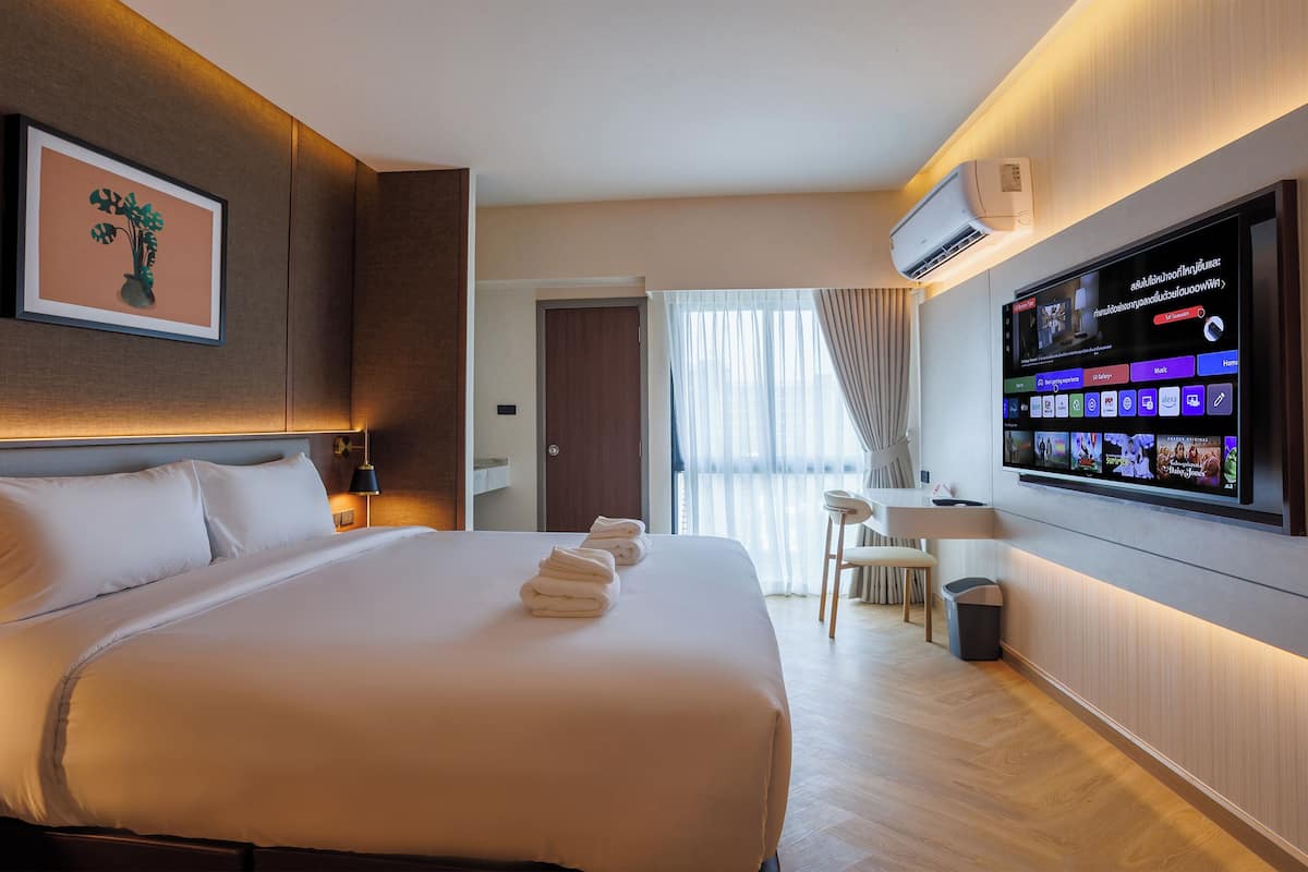 Una habitación de hotel moderna con una cama grande, un televisor de pantalla plana en la pared y una pequeña zona de escritorio.