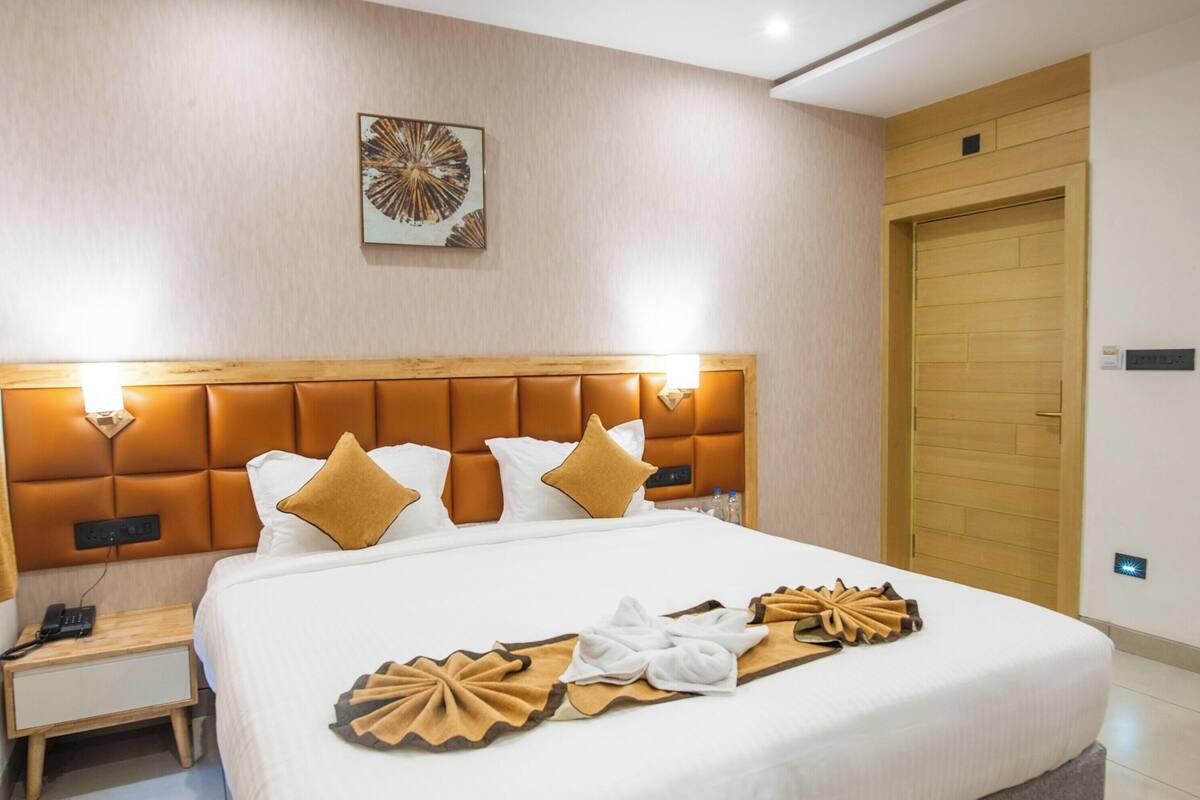 A hotel room with a large bed, a wooden headboard, bedside tables, a painting on the wall, and a wooden door.