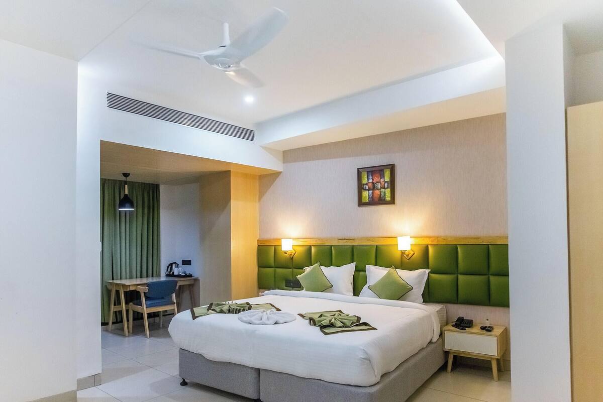 A hotel room with a bed, bedside table, desk, chair, and a ceiling fan.
