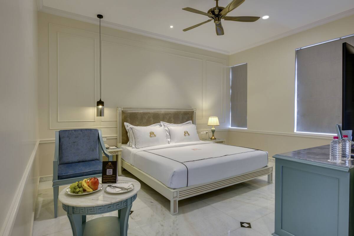 Habitación de hotel con cama, una silla, una mesita con fruta, una lámpara y un ventilador de techo.